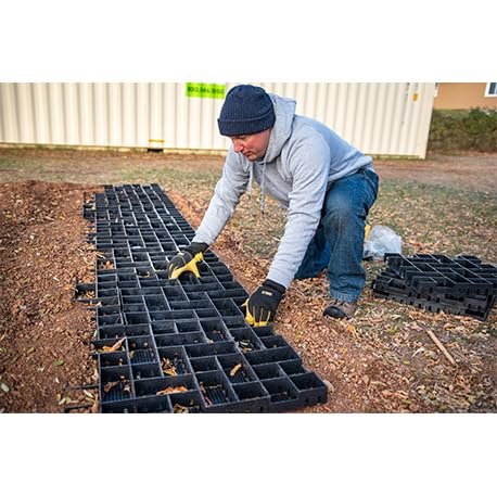 GEOBIN - Man kneeling on ground installing black GEOPAVE gravel porous paver panels on dirt surface outdoors