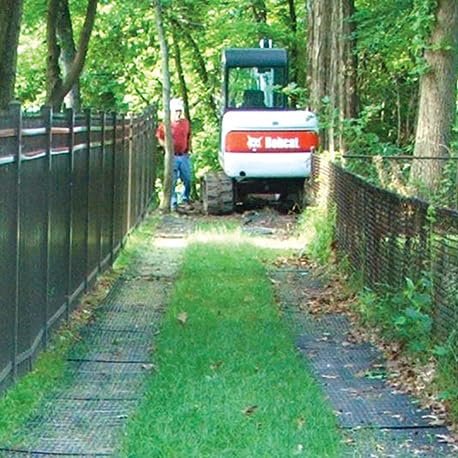 GEOBIN - Bobcat mini excavator driving over GEORUNNER black surface panels along fenced grass pathway between trees